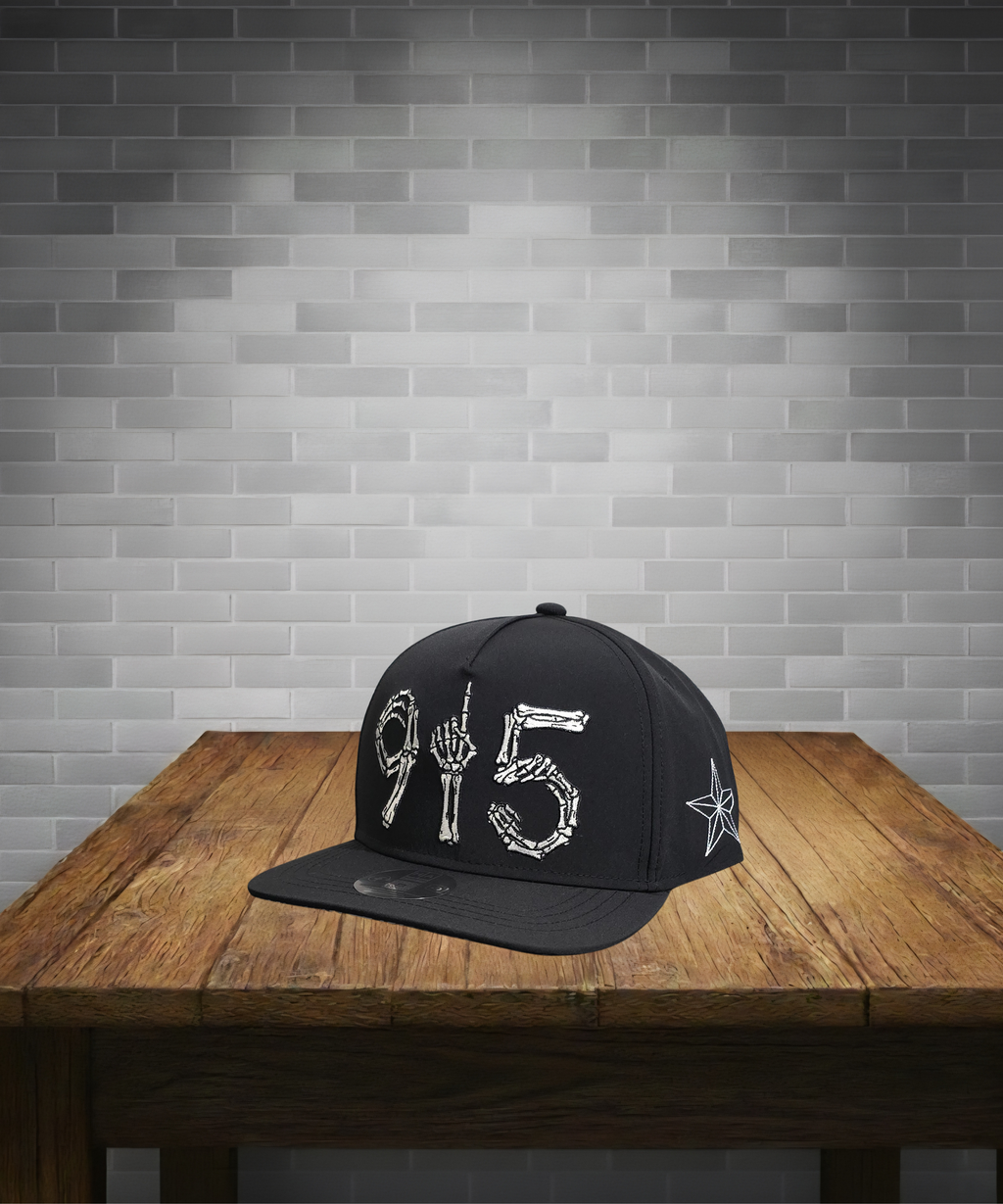 Black cap with white designs on a wooden table against a gray brick wall.