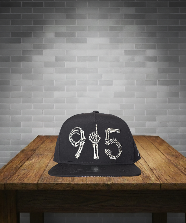 Black cap with white designs on a wooden table against a gray brick wall.