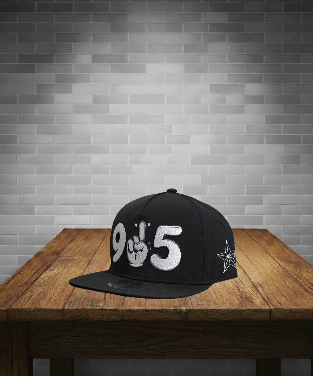 Black cap with white text and design on a wooden table against a gray brick wall.