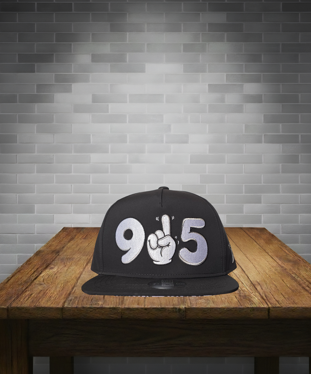 Black cap with '905' design on a wooden table against a gray brick wall.