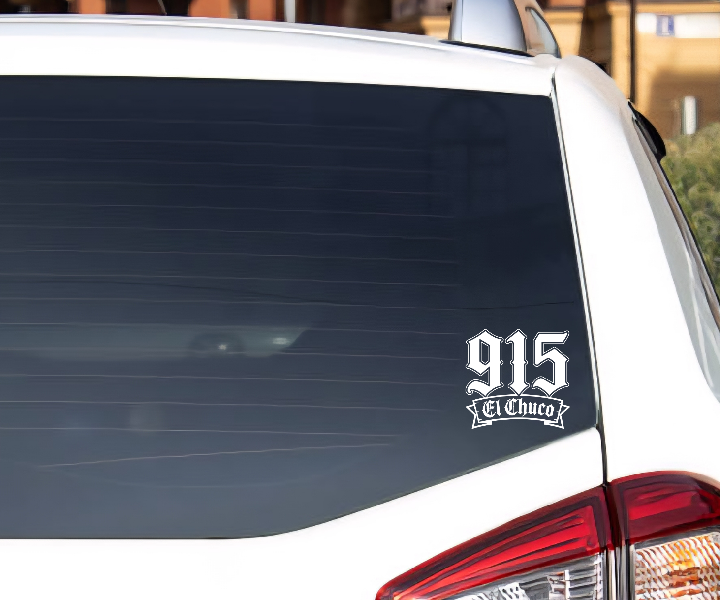 A white car rear window with a black heated tint and a white gothic-style decal that reads '915 El Chupo' on the lower right side of the window.