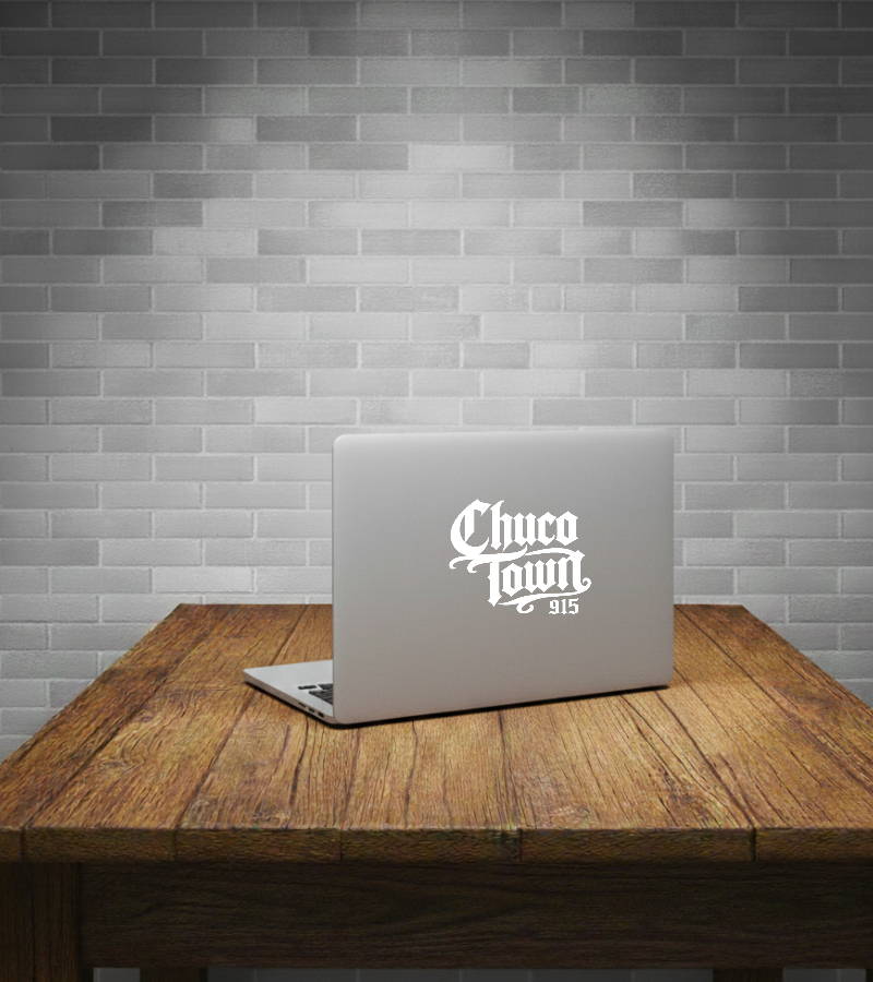 A silver laptop with a white 'Chuco Town 915' vinyl decal on the back, displayed on a rustic wooden table against a gray subway tile wall.