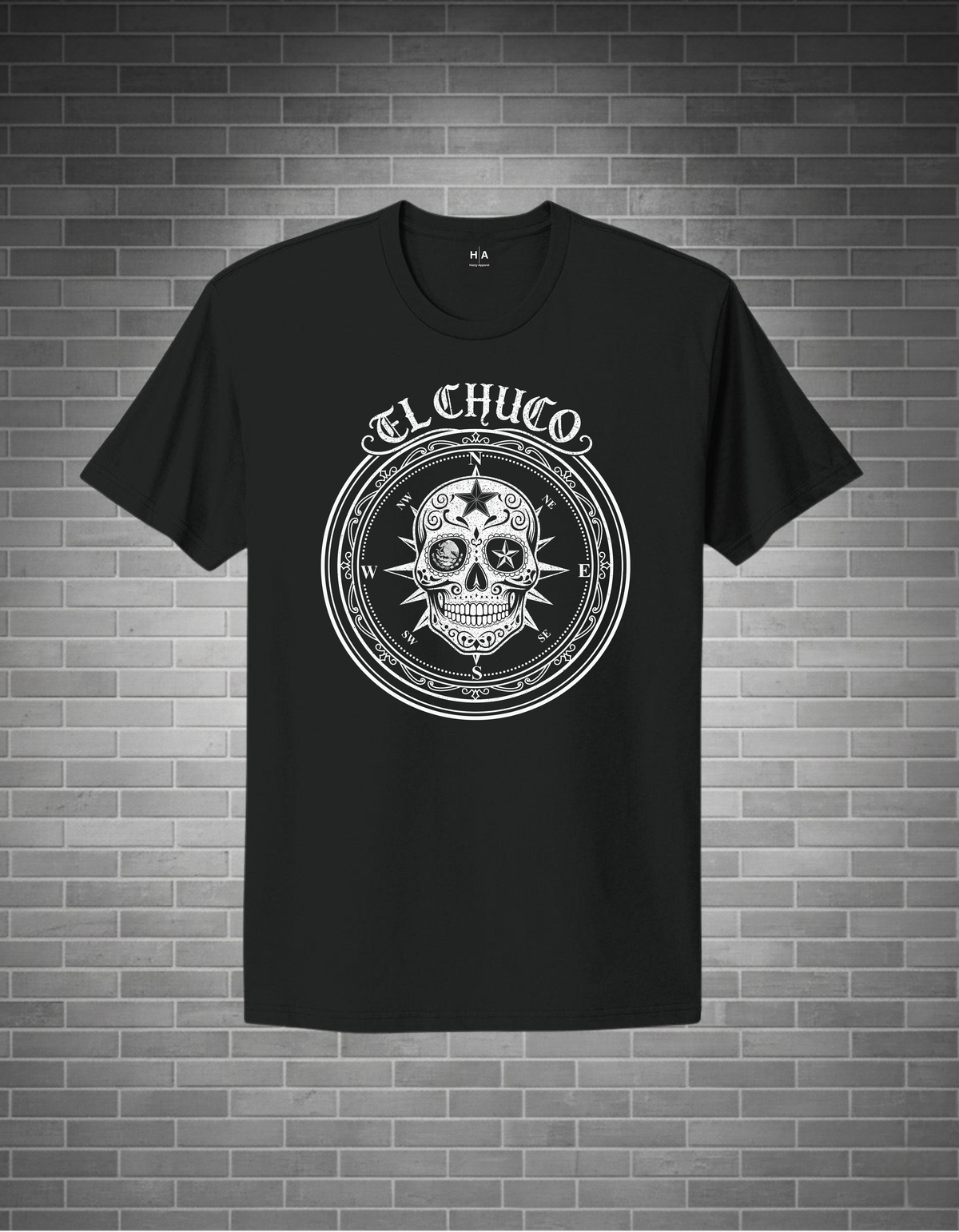 Black t-shirt with a white skull design and 'El Chuco' text on a brick wall background
