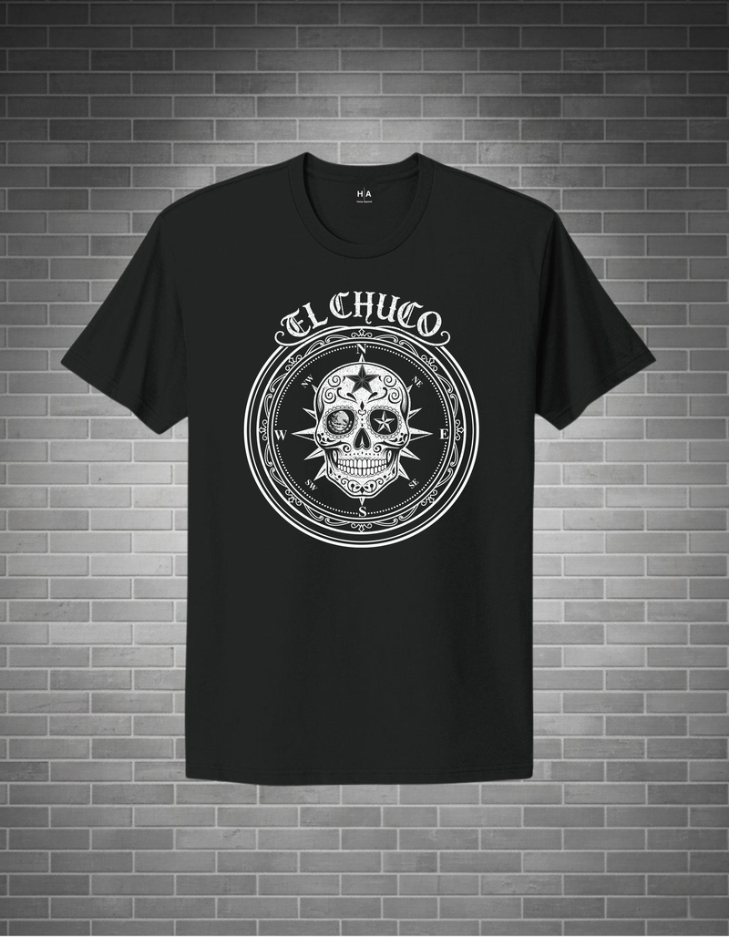 Black t-shirt with a white skull design and 'El Chuco' text on a brick wall background