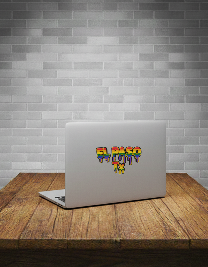 Laptop with a colorful 'El Paso TX' sticker on a wooden table against a gray tiled wall.