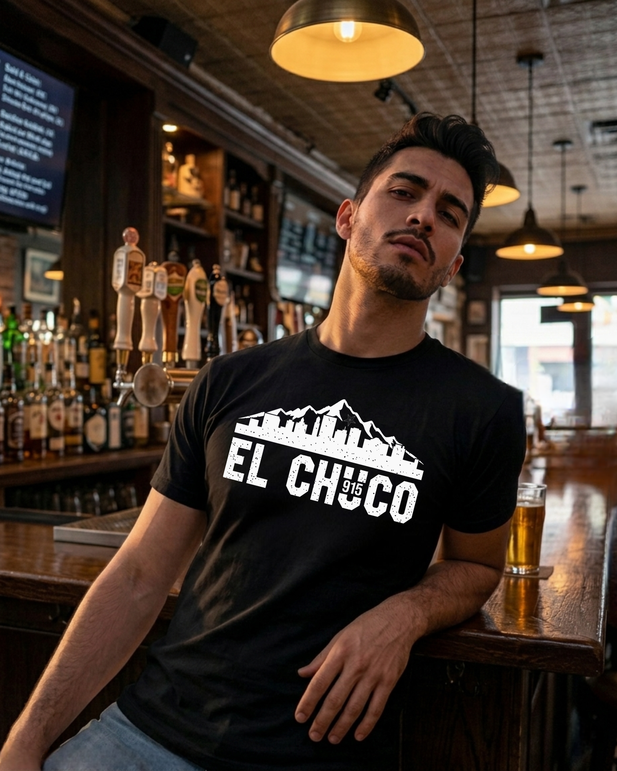 Man wearing a black t-shirt with 'El Chugo' logo in a bar setting