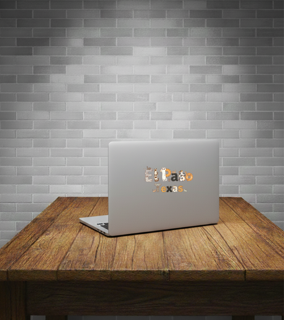 Laptop with 'El Paso Texas' sticker on a wooden table against a brick wall.