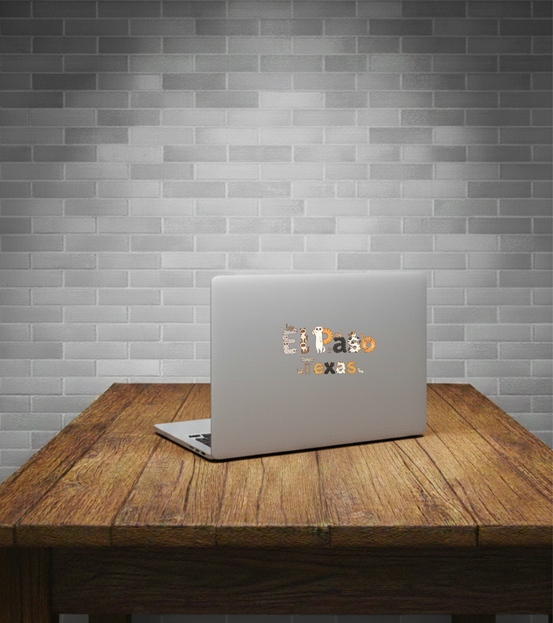 Laptop with 'El Paso Texas' sticker on a wooden table against a brick wall.