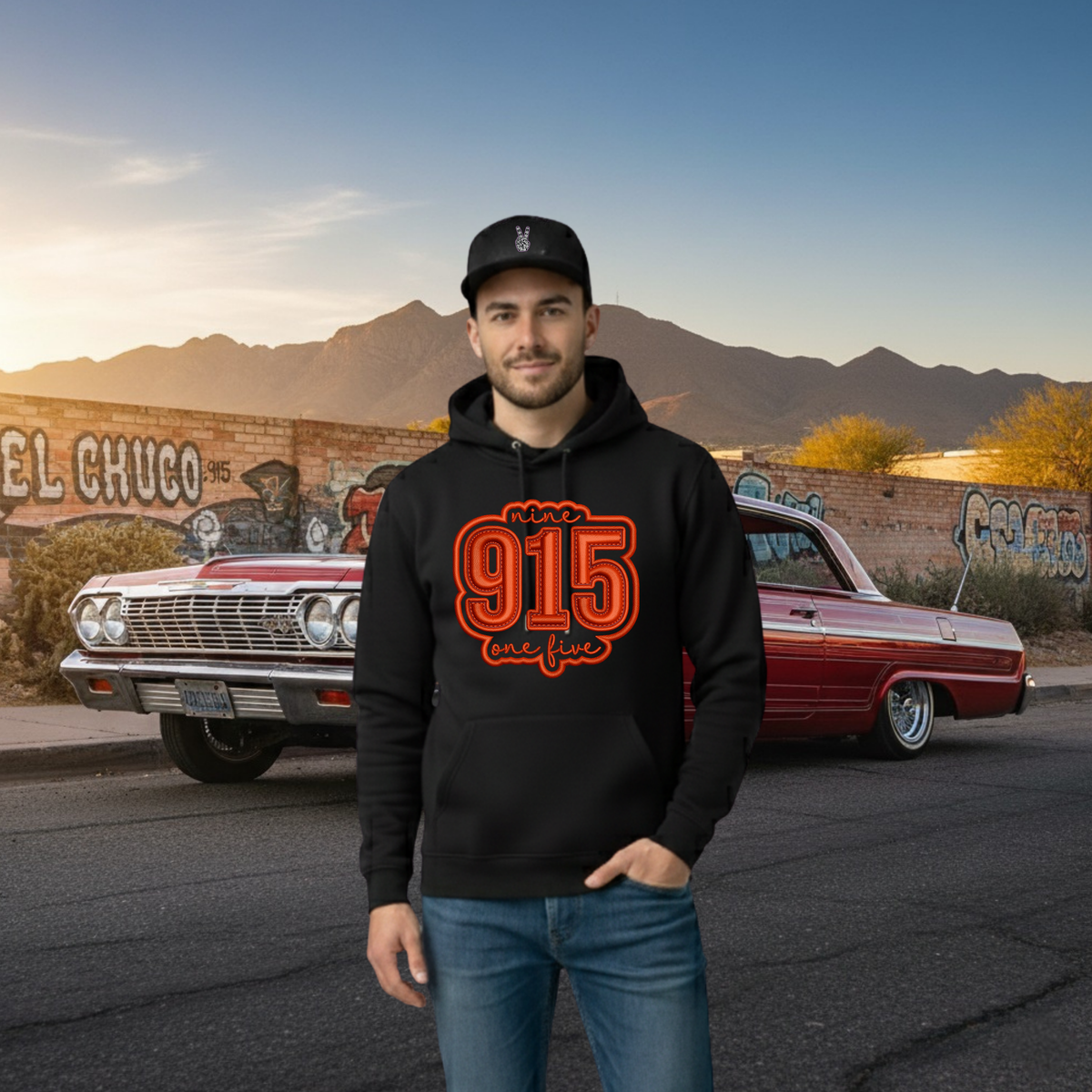 Man wearing a black hoodie with '915' design in front of a classic car and mural.