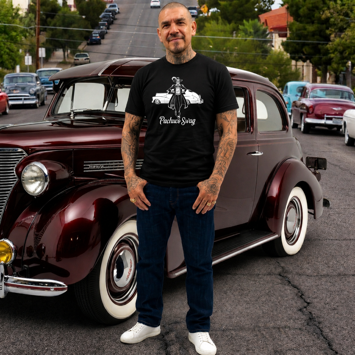 Man standing in front of a classic maroon car on a street with other vintage cars.