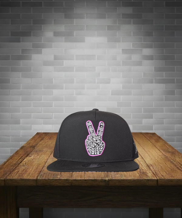 Black cap with a peace sign design on a wooden table against a gray brick wall.