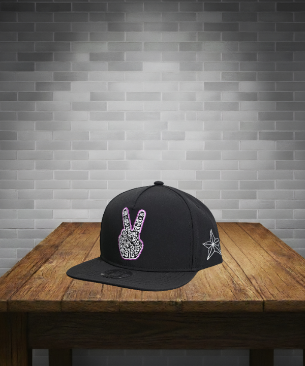 Black cap with peace sign design on a wooden table against a gray brick wall.