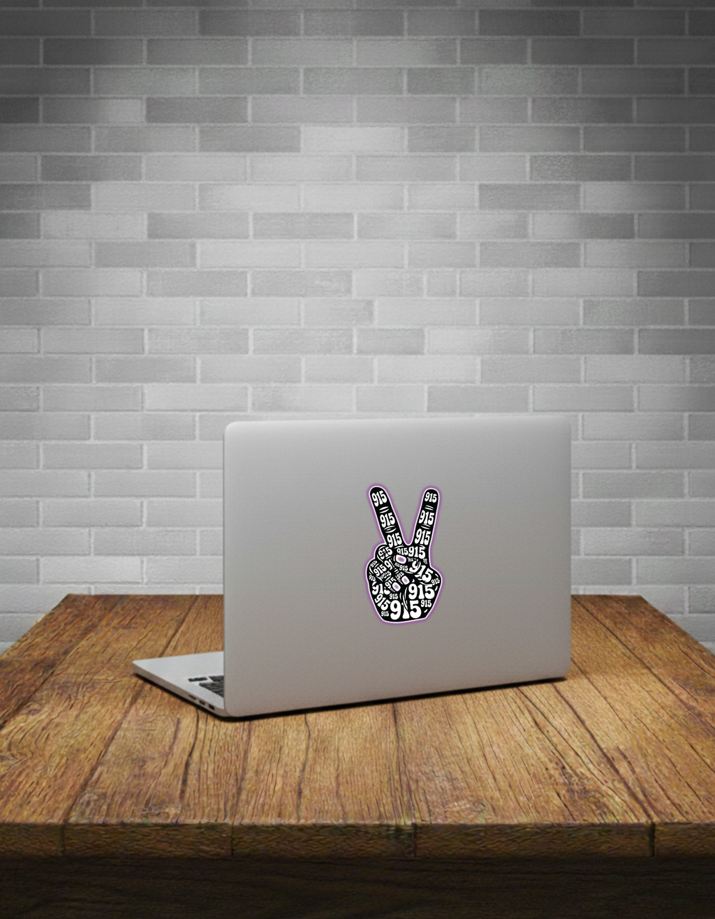 Laptop with a peace sign sticker on a wooden table against a grey brick wall.