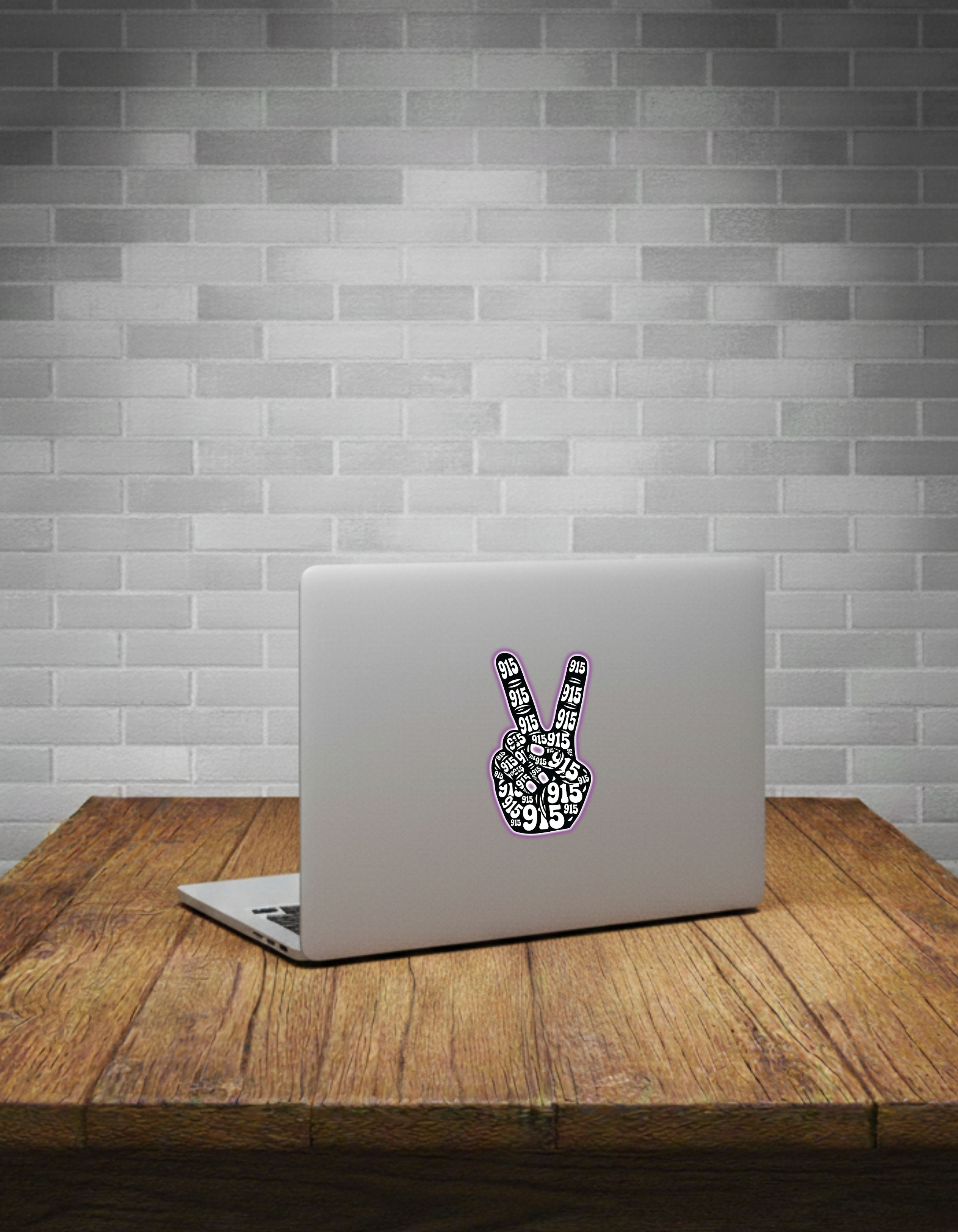 Laptop with a peace sign sticker on a wooden table against a grey brick wall.