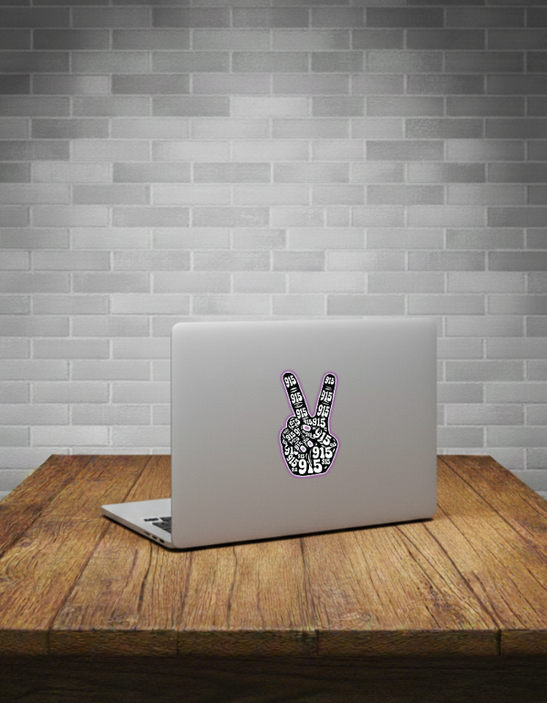 Laptop with a peace sign sticker on a wooden table against a grey brick wall.