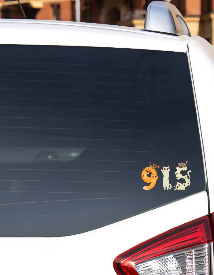 Car window with a decorative sticker featuring the numbers 915 and cat illustrations.