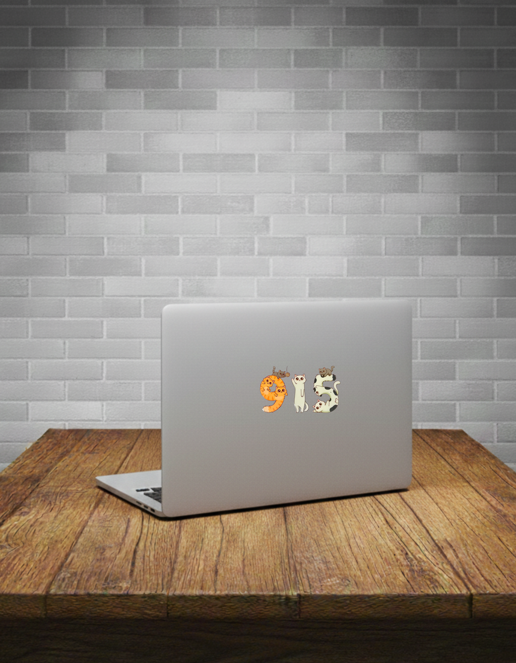 Laptop with a '915' cat sticker on a wooden table against a brick wall.