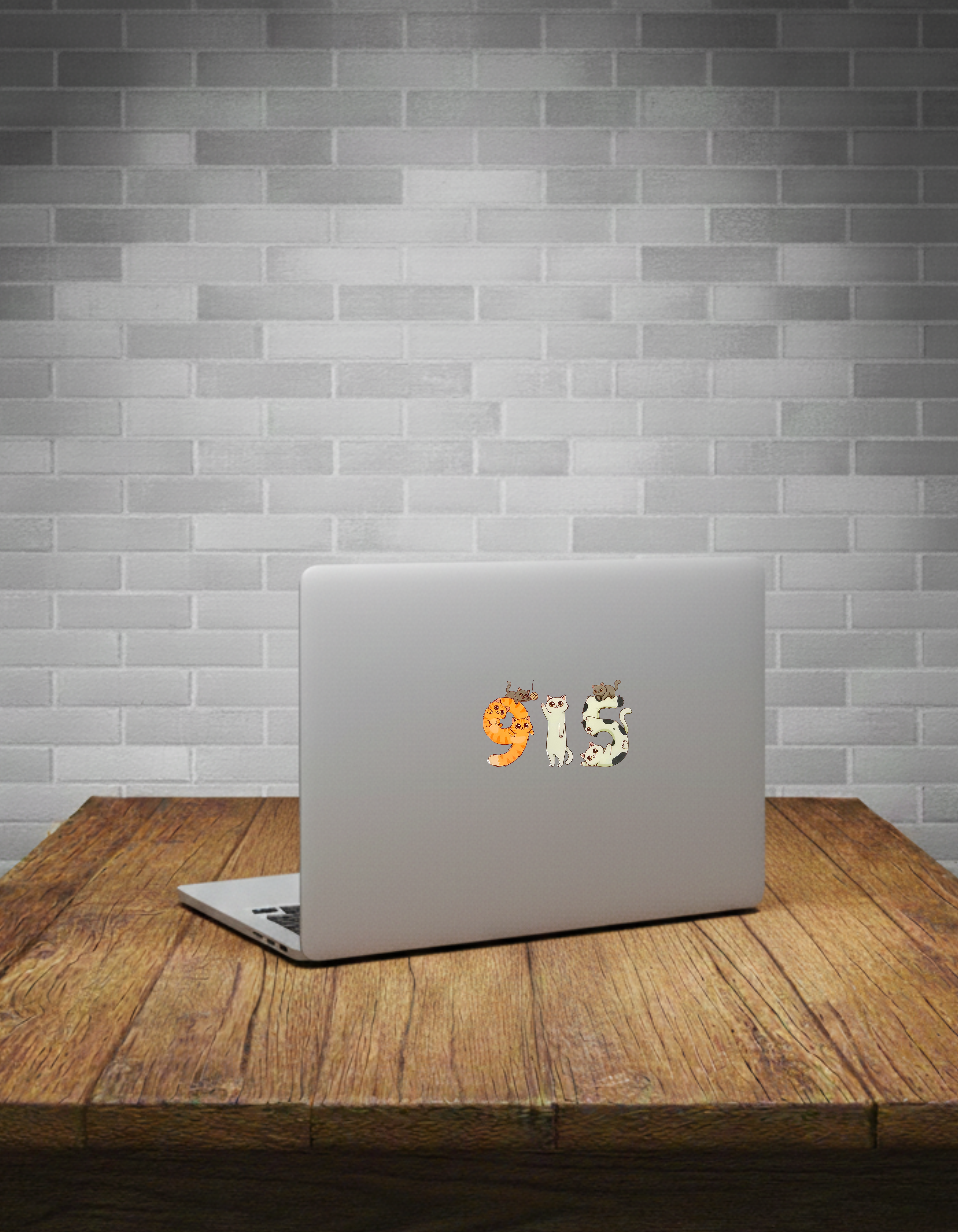 Laptop with a '915' cat sticker on a wooden table against a brick wall.