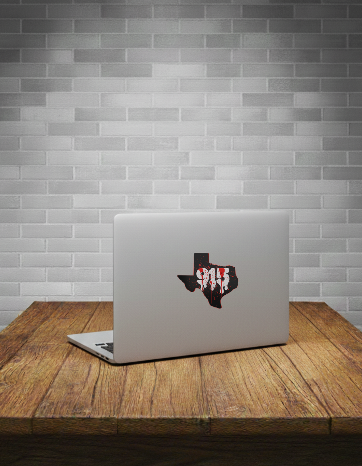 Laptop with a Texas-shaped red splatter sticker on a wooden table against a grey brick wall.