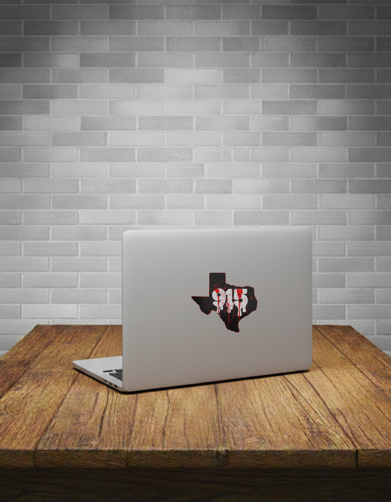 Laptop with a Texas-shaped red splatter sticker on a wooden table against a grey brick wall.