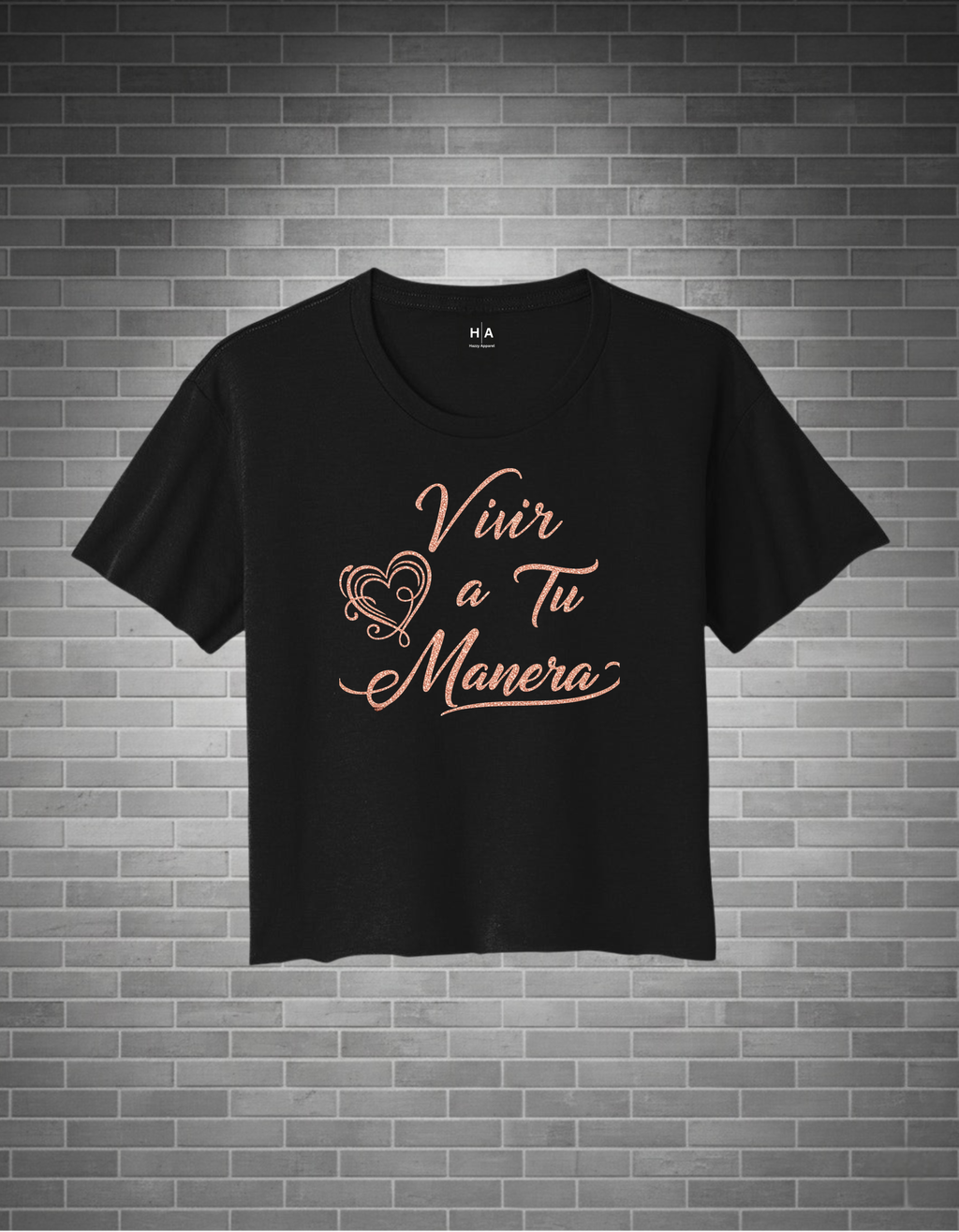 Black t-shirt with 'Vivir a Tu Manera' text on a brick wall background