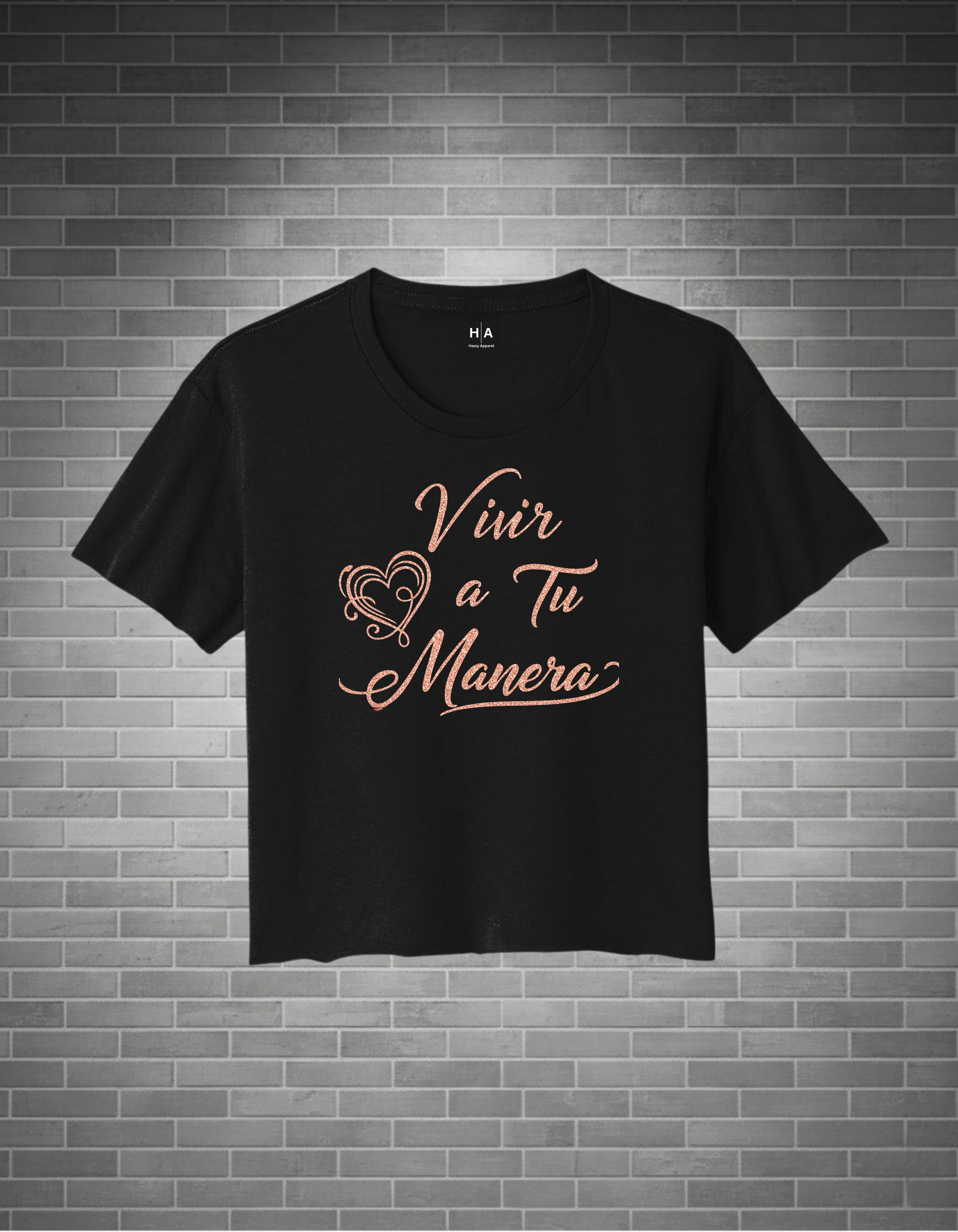 Black t-shirt with 'Vivir a Tu Manera' text on a brick wall background