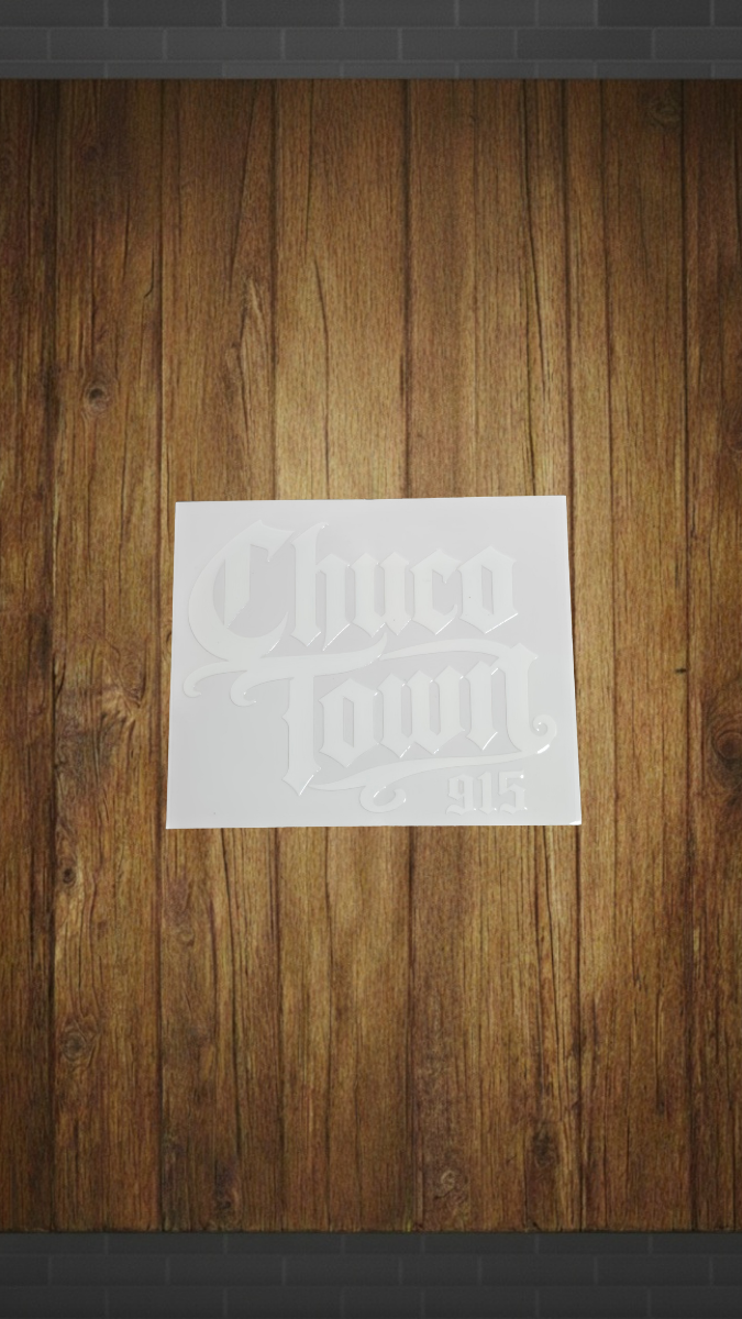 A white rectangular sticker or decal with embossed-style 'Chico Town 915' lettering, shown against a brown wood plank background.