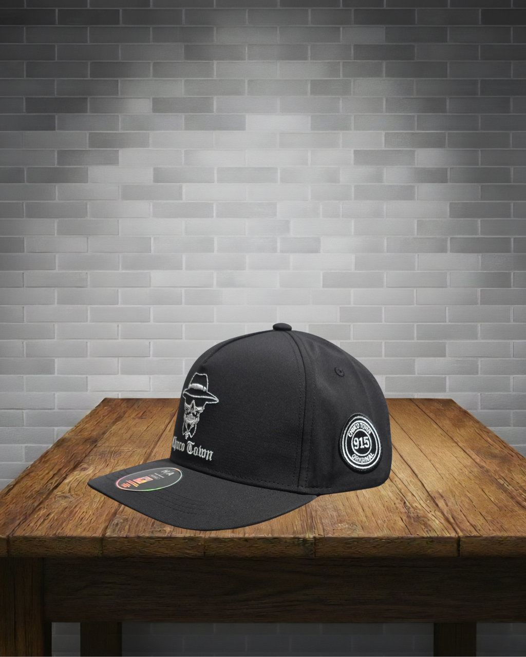 Black cap with white logo on a wooden table against a gray brick wall.