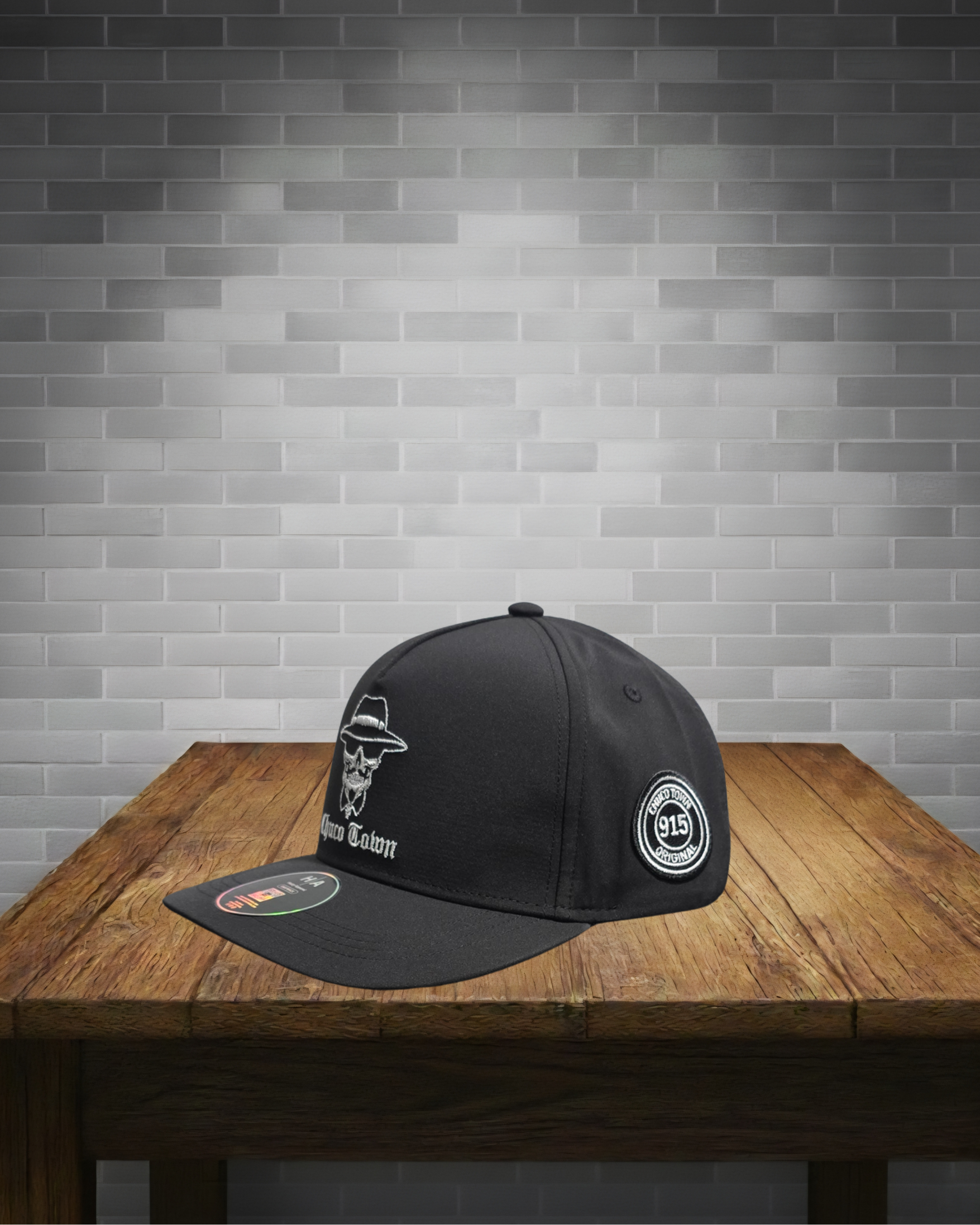 Black cap with white logo on a wooden table against a gray brick wall.
