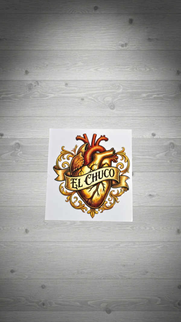 A square white sticker or print featuring a detailed anatomical heart illustration with gold decorative flourishes and a banner reading 'EL CHUCO', centered on a gray wood-plank background.