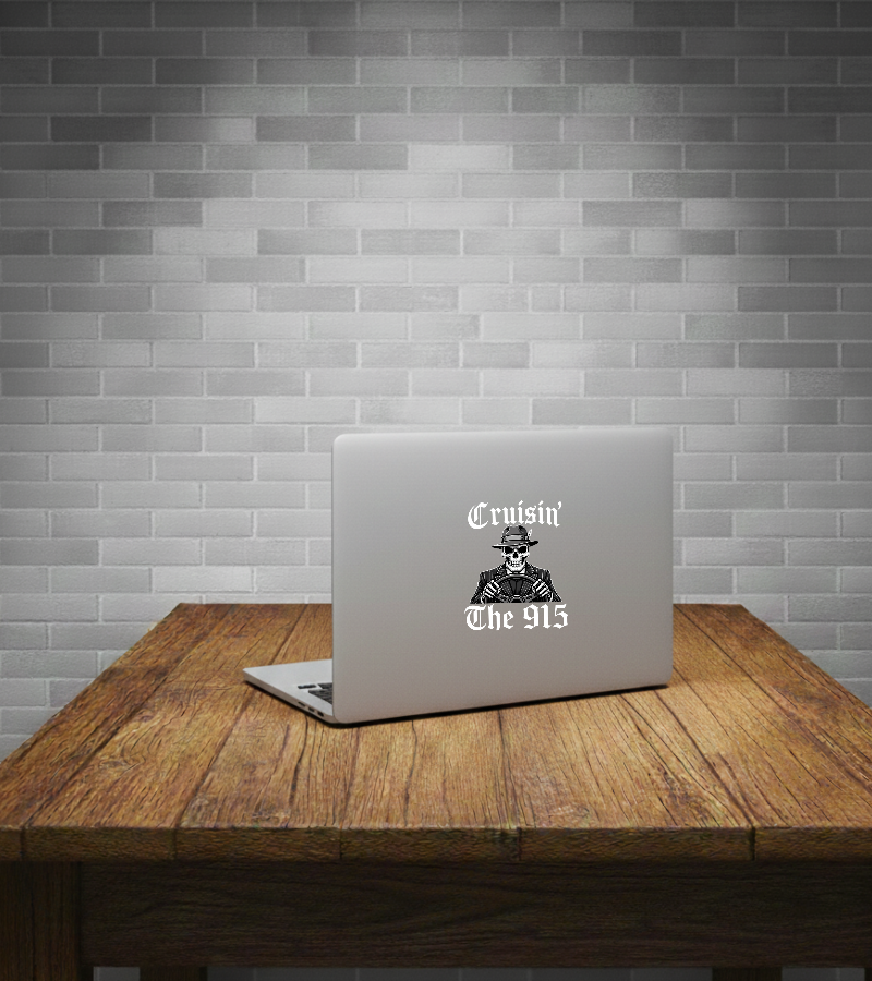 A silver laptop sits open on a rustic wooden table against a gray subway tile wall. The back of the laptop has a circular white sticker reading 'BORDERLAND CHOCO CREW' around a black illustrated face graphic.