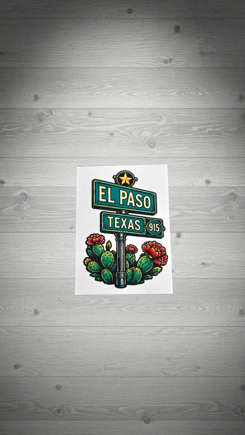 A rectangular art print featuring an illustrated street sign design with 'EL PASO' and 'TEXAS 915' signs, a star, cactus, and red flowers, displayed against a gray wood plank background.