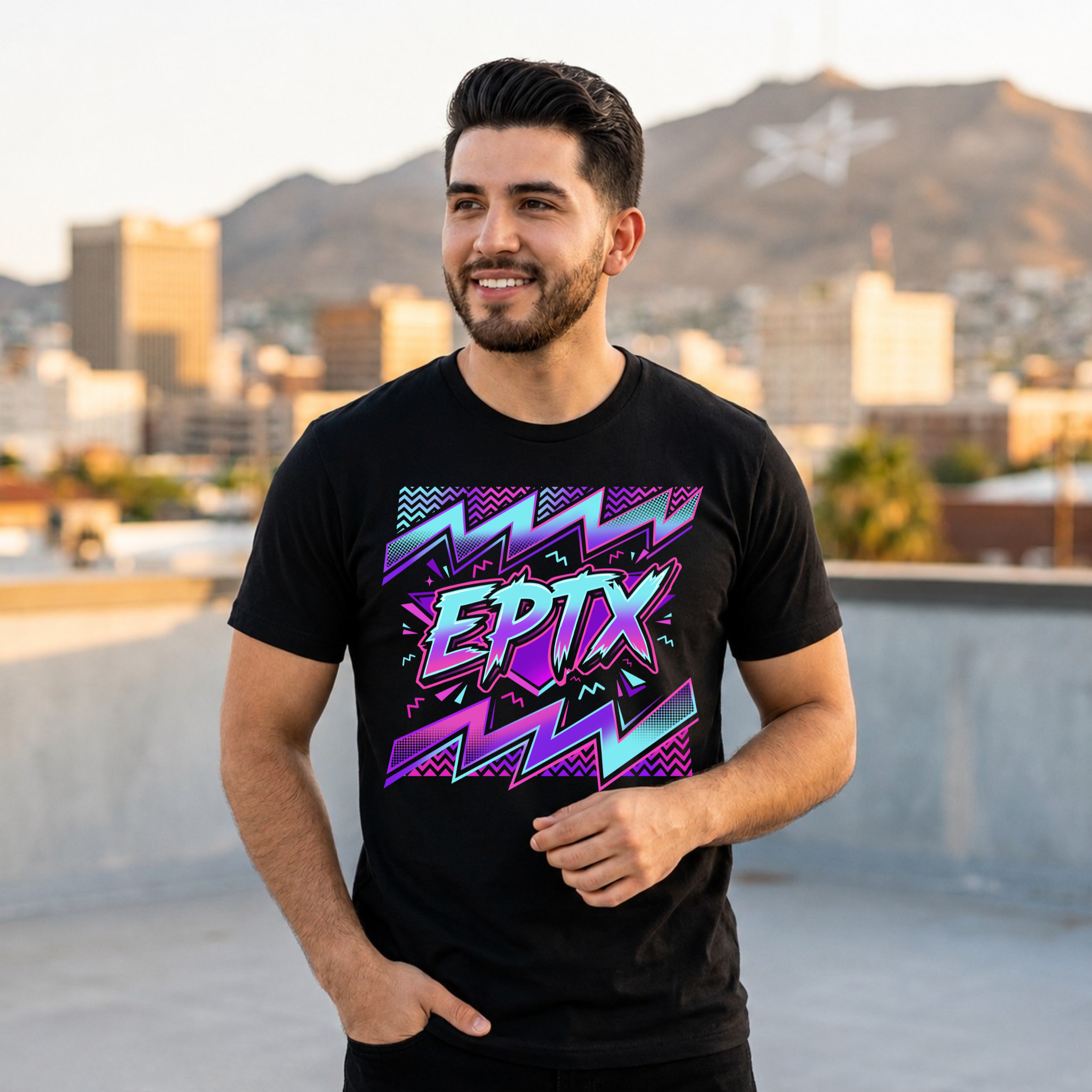 A man wearing a black t-shirt with a colorful 90s-style graphic that reads 'EPTX' in neon pink, purple, and blue, standing on a rooftop with a city skyline and mountains in the background.